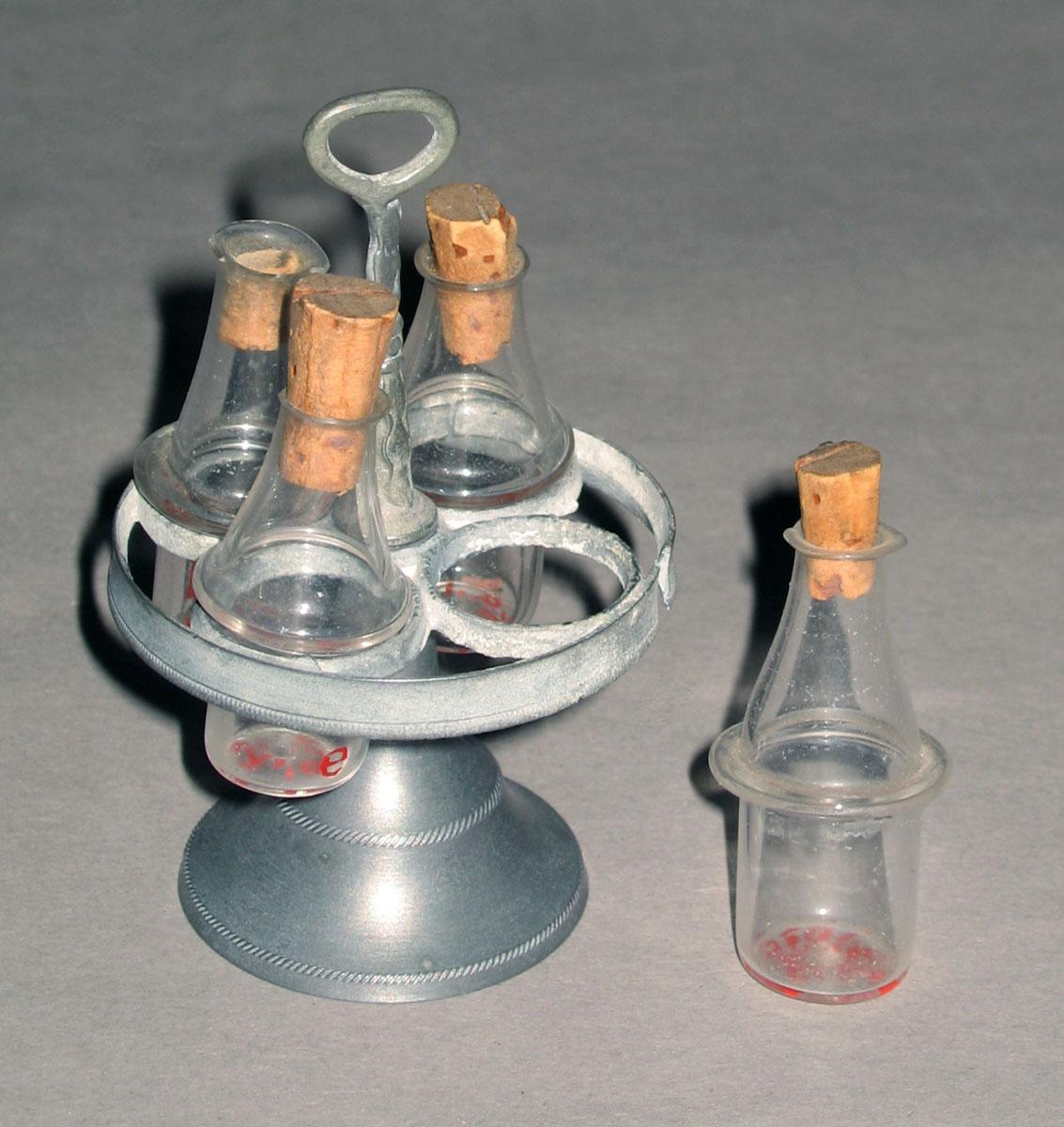 1959.1039 A- E Miniature metal cruet stand and glass bottles